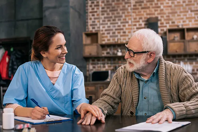 Smiling nurse reassuring an elderly man at his kitchen table